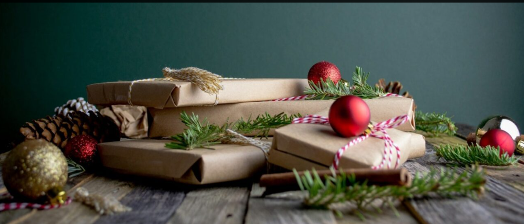 Gifts wrapped in brown paper with holiday orbs and pine needles.